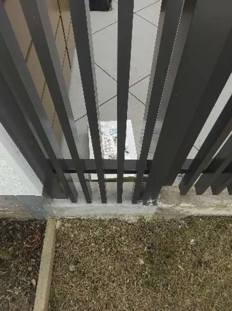 A wrapped parcel of printed flyers on the tiles behind a dark slatted front gate, seen from the garden outside.