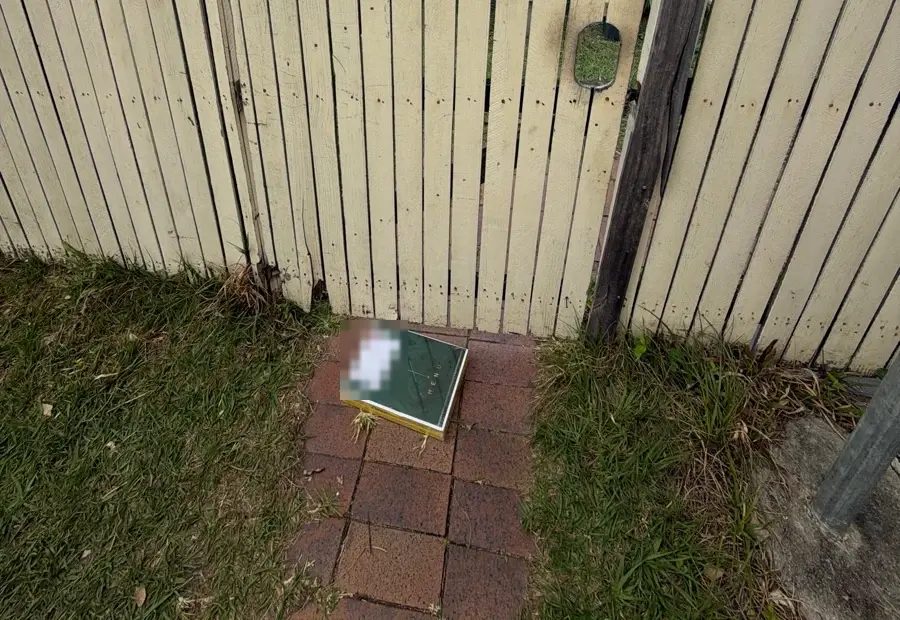 A green parcel of laminated menus on a brick path in front of a timber gate, delivery label blurred.