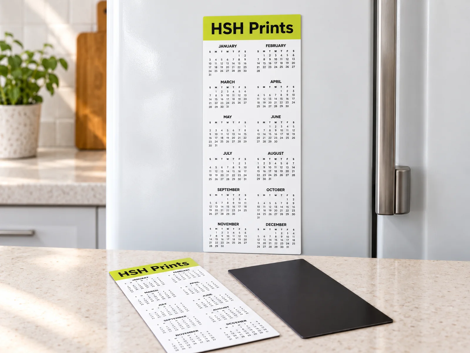 Mockup of an HSH Prints 2027 DL calendar magnet on a white fridge, with a second calendar and its magnetic back on the bench