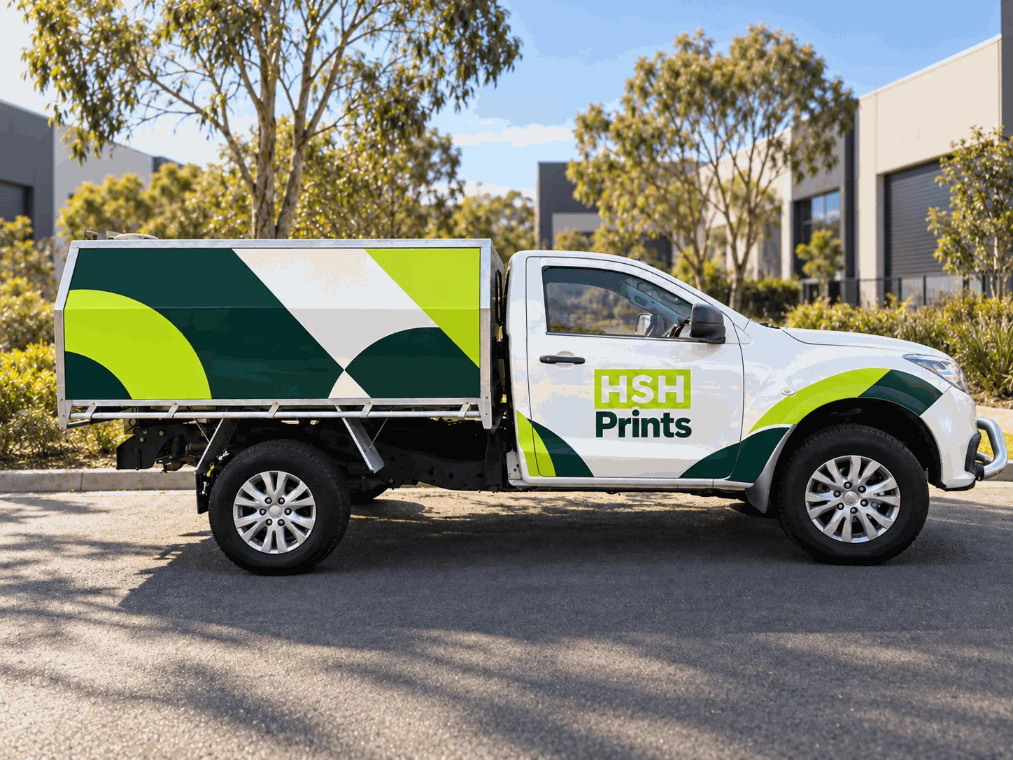 A white ute with the HSH Prints logo on the door, lime and green decal graphics sweeping over the front guard, and large geometric graphics covering the canopy