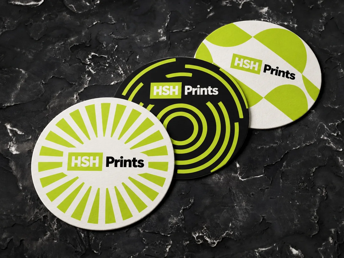 Mockup of three round HSH coasters in lime, white and black patterns on a dark stone surface