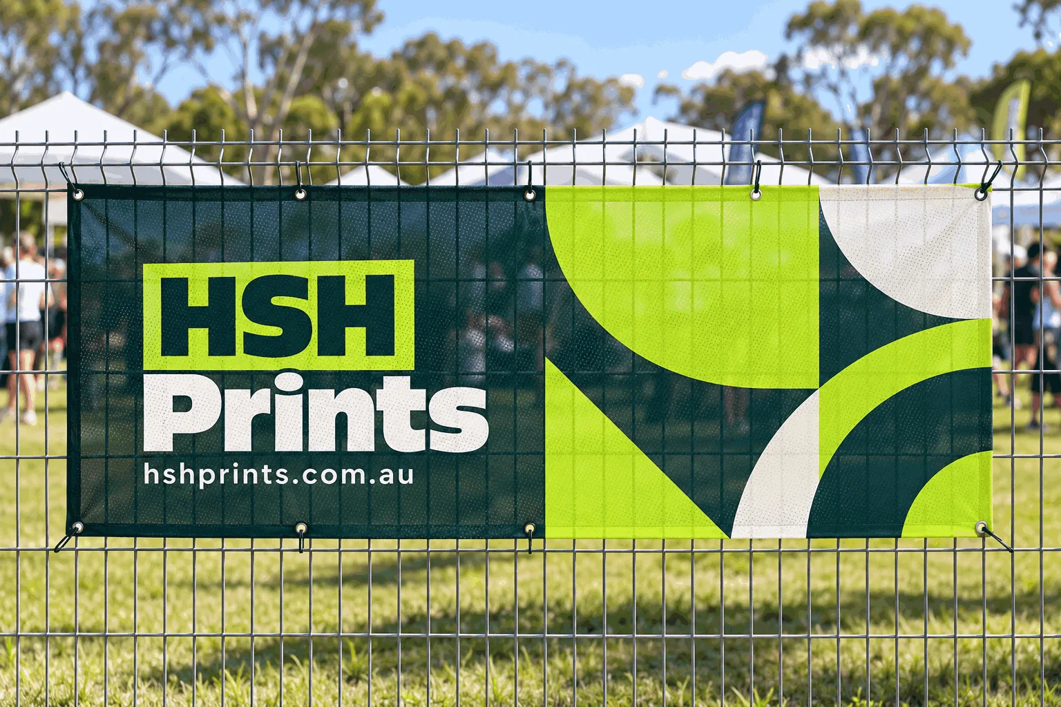 A printed mesh banner cable-tied to a wire fence at an outdoor event, the HSH Prints logo and web address on the left, the fence visible through the weave