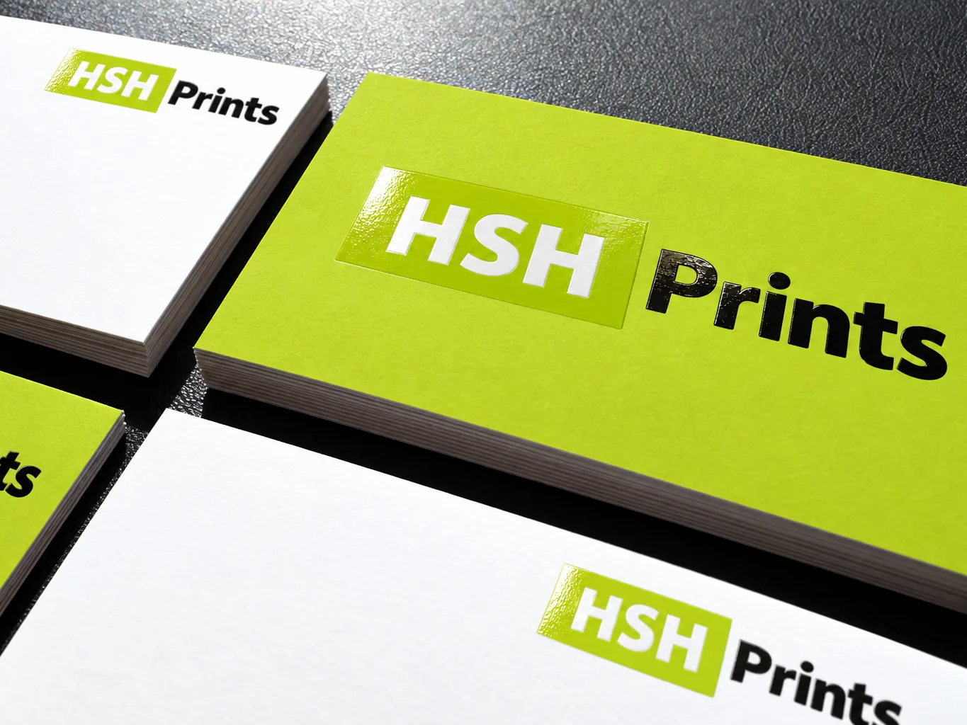 Mockup of premium HSH business cards on a dark surface, with a glossy spot UV logo raised on lime and white card