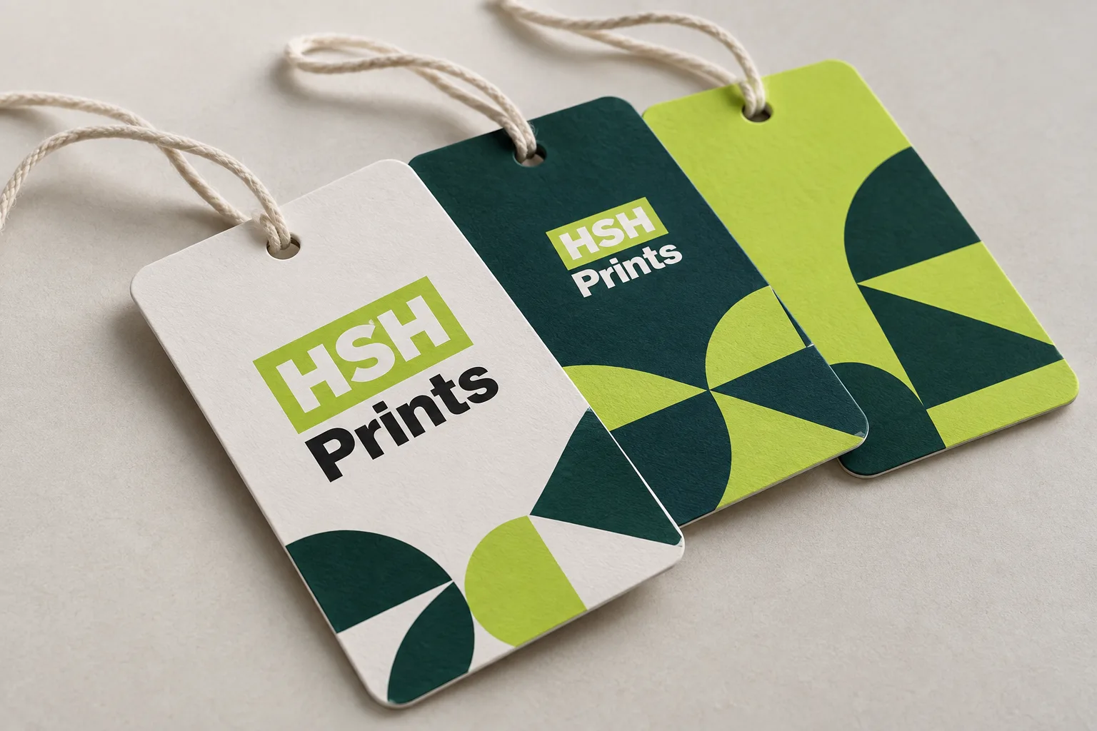 Three rectangle swing tags with rounded corners, white, dark green and lime, on cotton string, laid on a pale surface