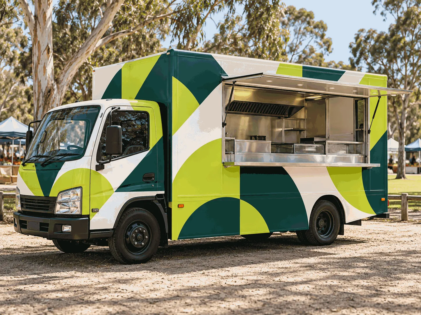 A food truck wrapped in large lime, deep green and white geometric shapes, parked at a market with its serving hatch open