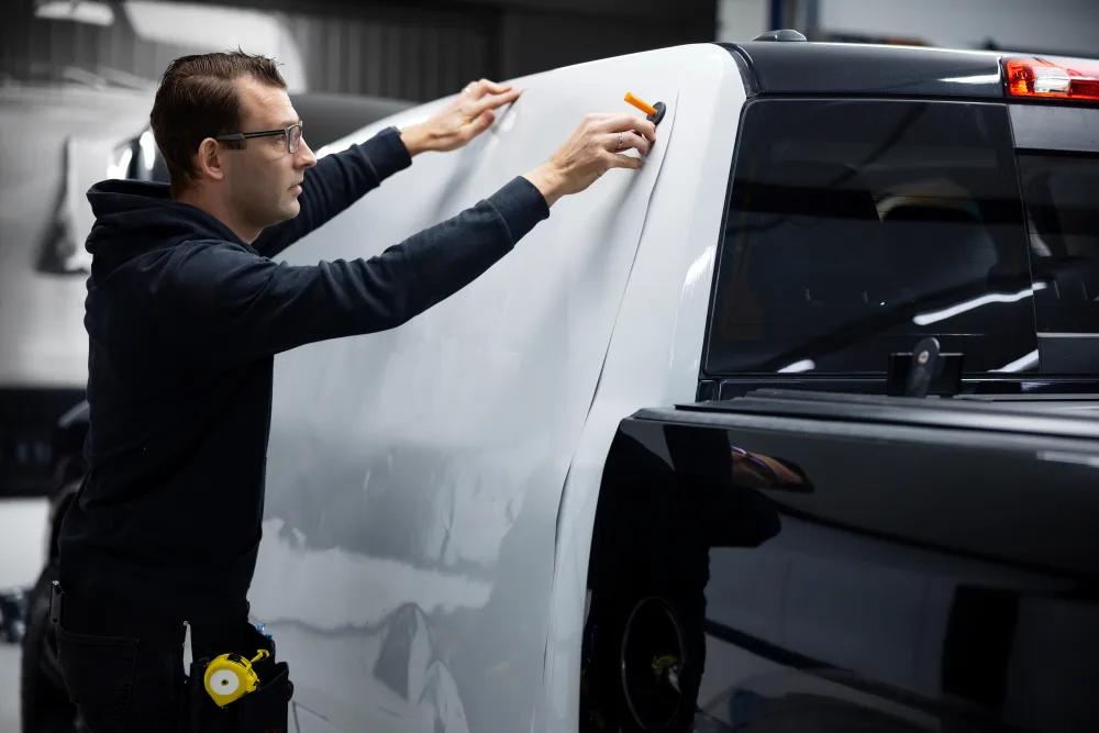 An installer squeegeeing white wrap vinyl down the rear pillar of a dual-cab ute in a workshop bay