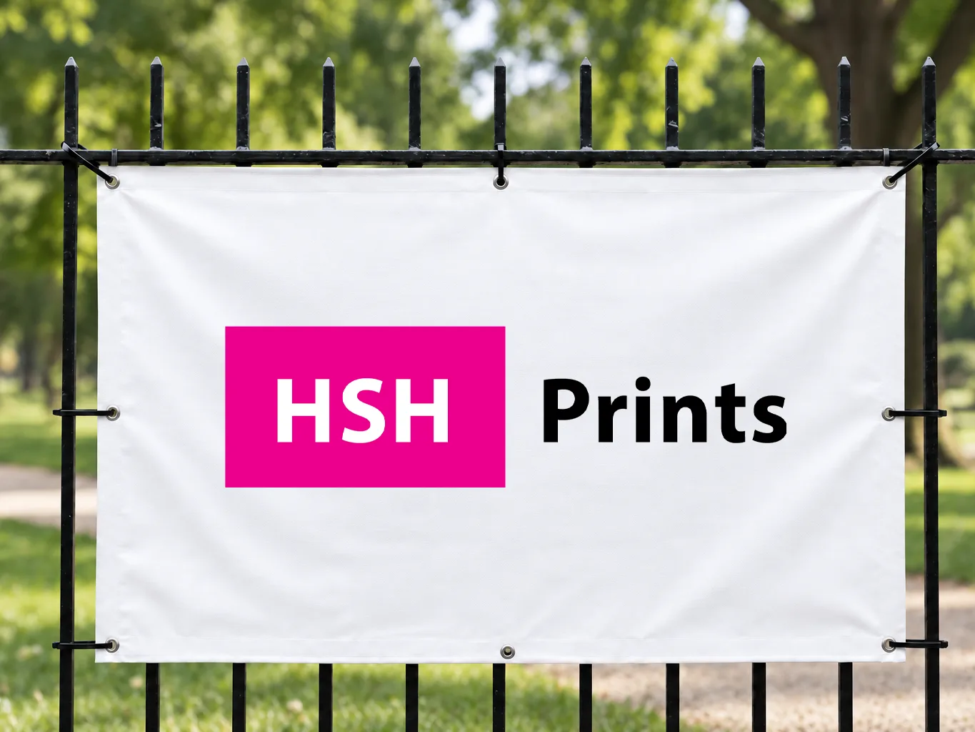 Mockup of a white vinyl banner with the HSH logo in magenta, cable-tied through its eyelets to a black steel fence in a park